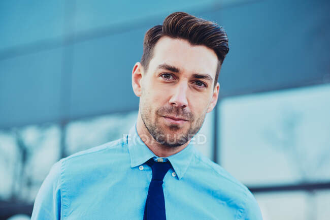 Exécutif masculin barbu en chemise formelle et cravate en ville en regardant la caméra sur fond flou — Photo de stock