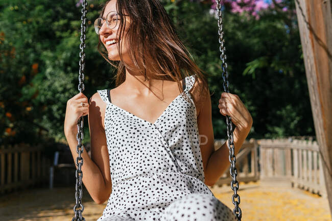 Вид на урожай веселой молодой женщины в очках, качающейся в парке в солнечный летний день — стоковое фото