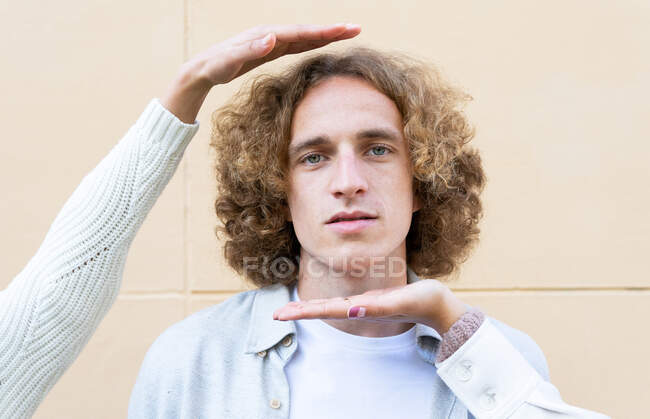 Crop female hands framing face of young man with curly hair looking calmly at camera — Stock Photo