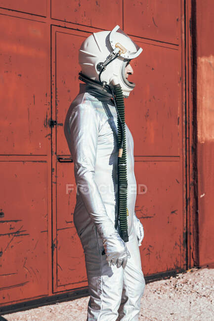 Hombre en traje espacial de pie cerca de la pared roja de la instalación industrial en el día soleado - foto de stock