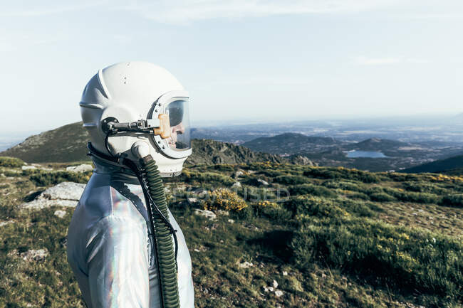 Side view male astronaut in spacesuit and helmet standing on grass and stones in highlands — Stock Photo