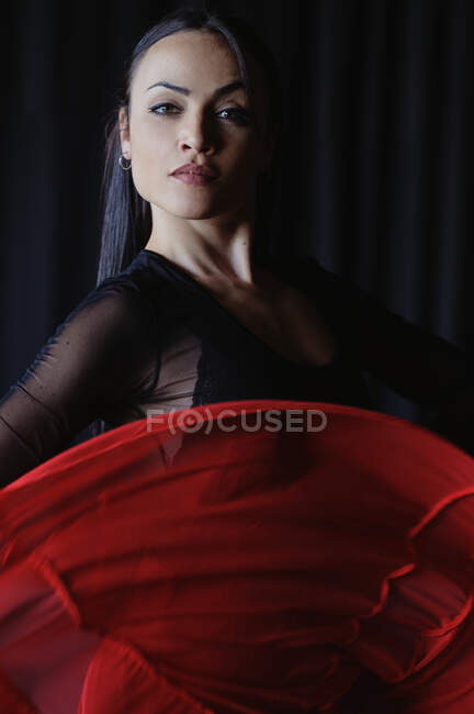 Молодая женщина с макияжем в красной и черной одежде исполняет традиционный испанский танец, глядя в камеру — стоковое фото