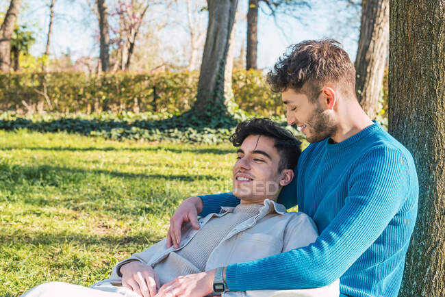 Fröhliche LBGT paar Männer umarmen sich, während sie im Park sitzen und einander anschauen — Stockfoto