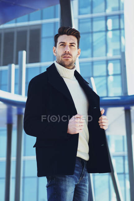 Homme barbu adulte en pull et manteau se promenant tout en regardant loin dans la ville en journée — Photo de stock
