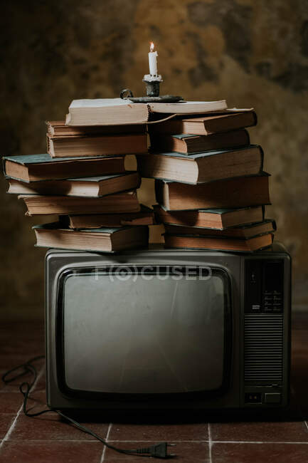 Montón de libros colocados en la parte superior de la televisión vintage con candelabro encendido en el suelo de baldosas de mala calidad - foto de stock