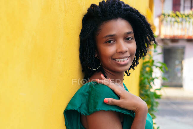 Close upside portrait of beautiful smiling young Black woman leaning against wall outside — Stock Photo