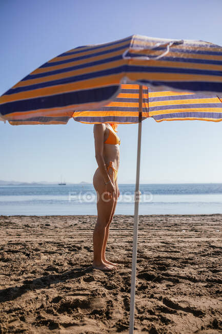 Vista lateral de una joven pelirroja anónima parada en la playa en un día soleado en verano - foto de stock