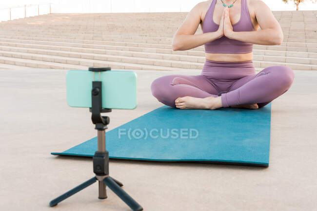 Cultiver femme anonyme assis dans la pose Lotus et pratiquer le yoga sur tapis avec téléphone mobile — Photo de stock