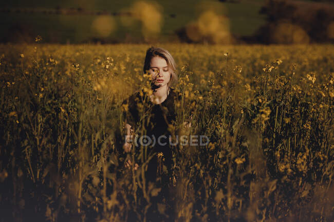 Portrait d'une belle jeune femme à la campagne avec les yeux fermés parmi les fleurs — Photo de stock