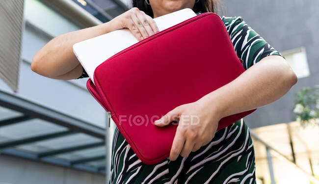 From below of anonymous plus size young female student in stylish outfit taking laptop of red case on urban background — Stock Photo