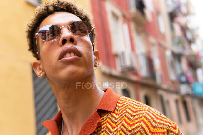 Low angle of confident young ethnic male tourist looking away while exploring old narrow streets of Barcelona city — Stock Photo