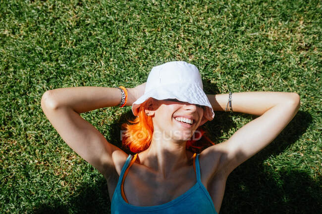 Draufsicht auf junge fröhliche rothaarige Frau, die an einem sonnigen Sommertag im Gras liegt — Stockfoto