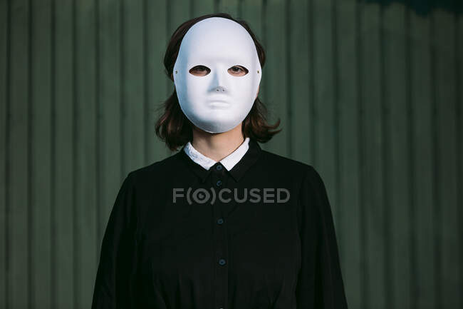 Spooky anonymous female in white Halloween mask standing in city — Stock Photo