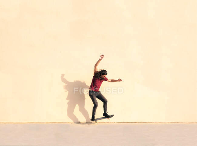 Male skateboarder with wavy hair performing trick on skateboard while jumping over walkway and looking down on sunny day — Stock Photo