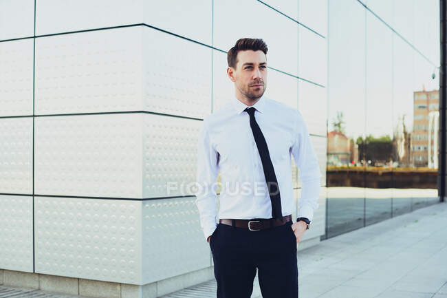 Homme entrepreneur en tenue formelle avec les mains dans les poches regardant loin en ville — Photo de stock