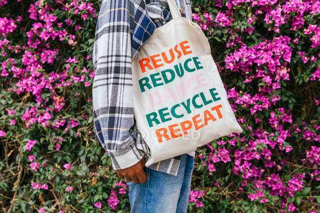 Vista laterale del maschio afroamericano irriconoscibile ritagliato in piedi con shopping bag eco-friendly nel giardino estivo in fiore — Foto stock