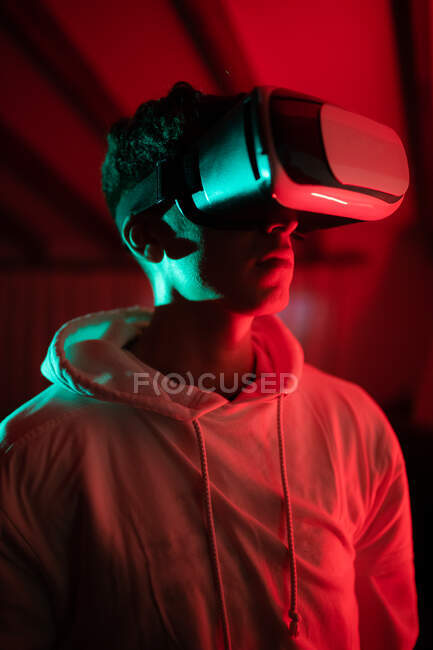 Чоловік в светрі під час використання VR окулярів і стоячи в студії з червоними неоновими вогнями — стокове фото