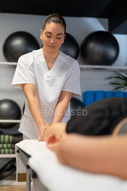 Счастливая массажистка в белом халате массирует телёнка урожая пациентка во время сеанса физиотерапии в клинике — стоковое фото