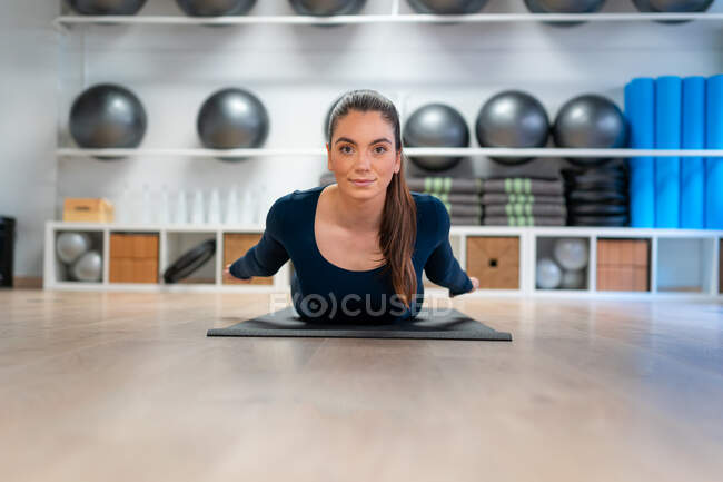 Cuerpo completo de joven hembra haciendo pose de langosta mientras practica yoga en estudio mirando la cámara - foto de stock