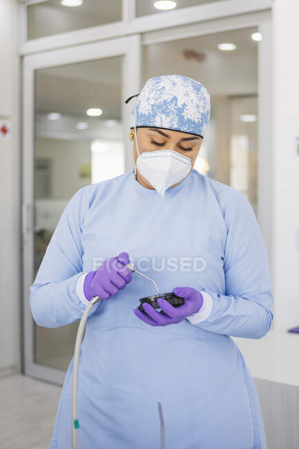 Adult female doctor in uniform and respiratory mask with small plate and water gun during cleaning process in clinic — Stock Photo