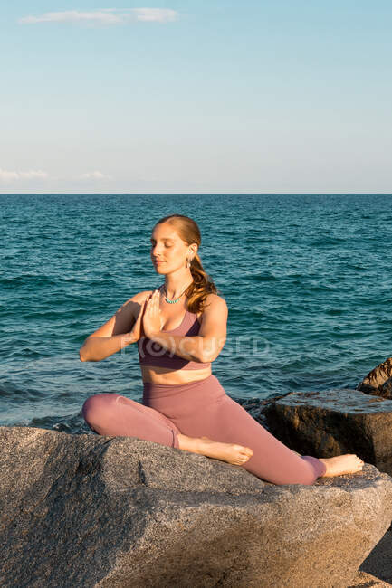 Pacifico flexível feminino praticando ioga em Eka Pada Rajakapotasana na rocha na praia — Fotografia de Stock
