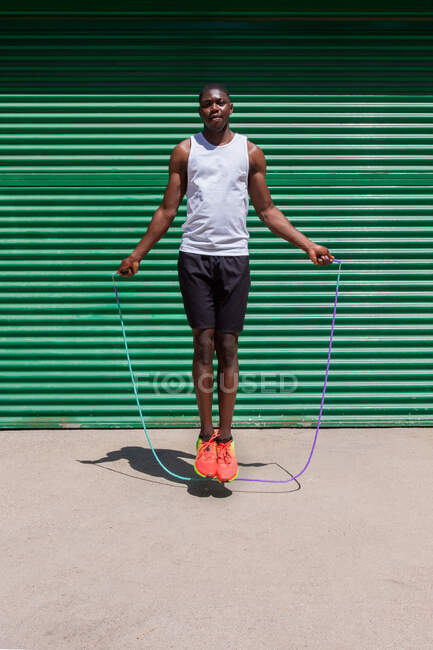 Focused African American male athlete jumping rope during cardio workout on sunny day in city — Stock Photo