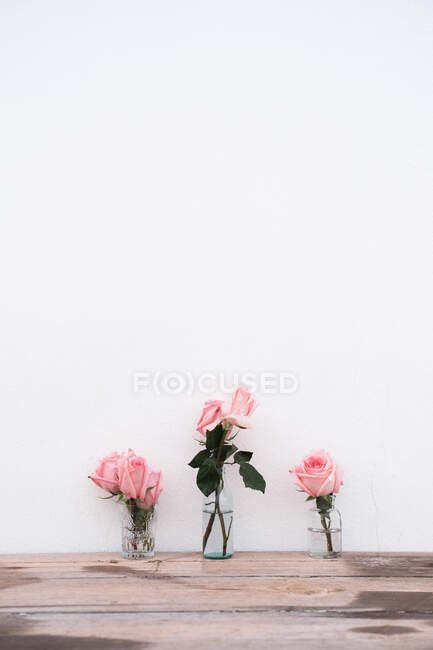 Rosarote Rosen in Glasvasen auf Holzoberfläche vor neutralem Hintergrund — Stockfoto