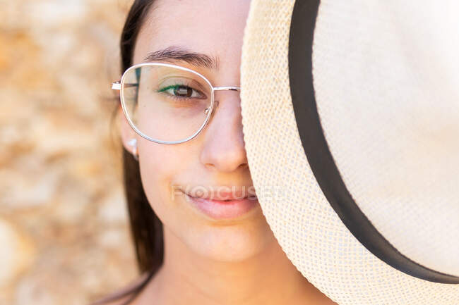 Close up portrait of young woman in glasses covering half face with a hat while looking at camera — Stock Photo