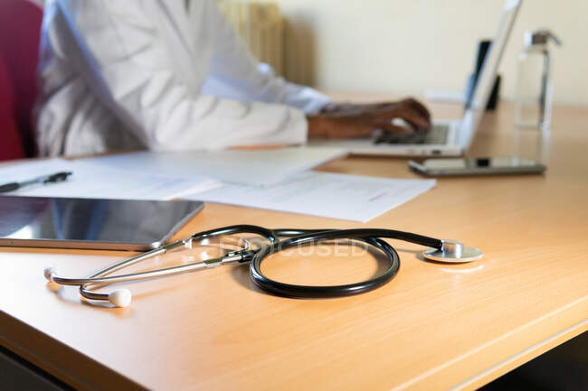Ernte afroamerikanische Ärztin tippt Bericht auf Laptop, während sie am Tisch in modernem Klinikbüro arbeitet — Stockfoto