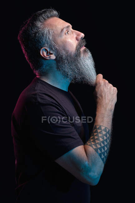 Side view of handsome mature male with gray beard on black background in studio — Stock Photo