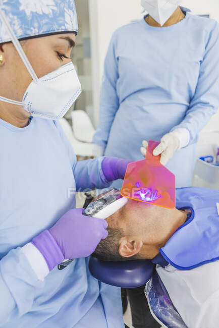 Высокий угол у врача в форме в стерильных перчатках и маске и лечении зубов с помощью зубного инструмента с ассистентом — стоковое фото