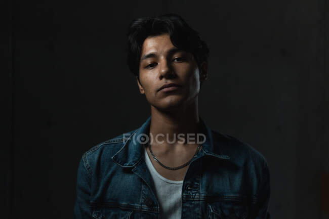 Porträt eines jungen lateinischen Mannes, der unter dramatischer Beleuchtung und dunklem Hintergrund selbstbewusst in die Kamera blickt — Stockfoto
