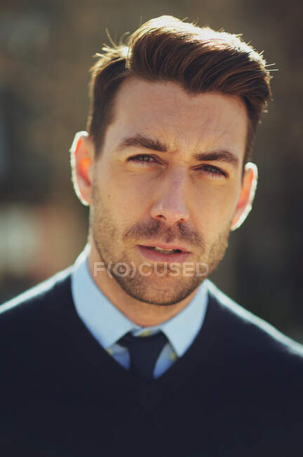 Empreendedor masculino barbudo com corte de cabelo moderno olhando para a câmera na cidade na parte traseira iluminada — Fotografia de Stock