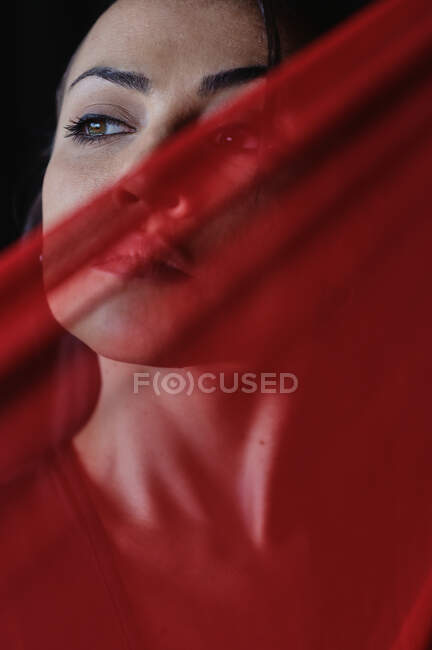 Куст молодая женщина с красными губами, глядя в сторону прозрачного текстиля с складками — стоковое фото