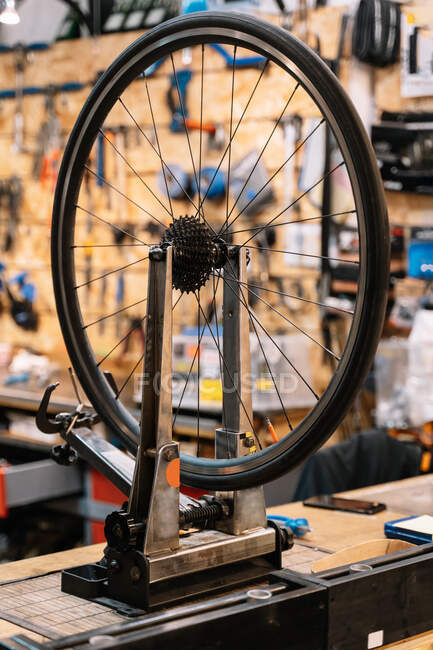 Bicycle wheel on metal truing stand placed on workbench in repair service workshop — Stock Photo