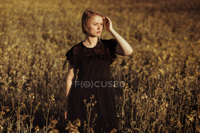 Porträt einer schönen jungen Frau, die auf dem Land zwischen Blumen wegschaut — Stockfoto