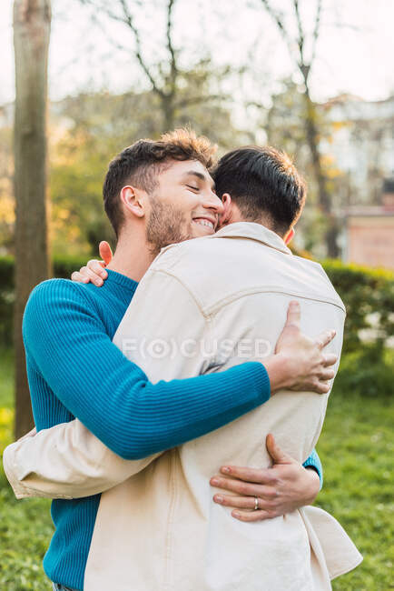 Alegre LGBT casal de machos abraçando enquanto de pé no parque no ensolarado dia — Fotografia de Stock