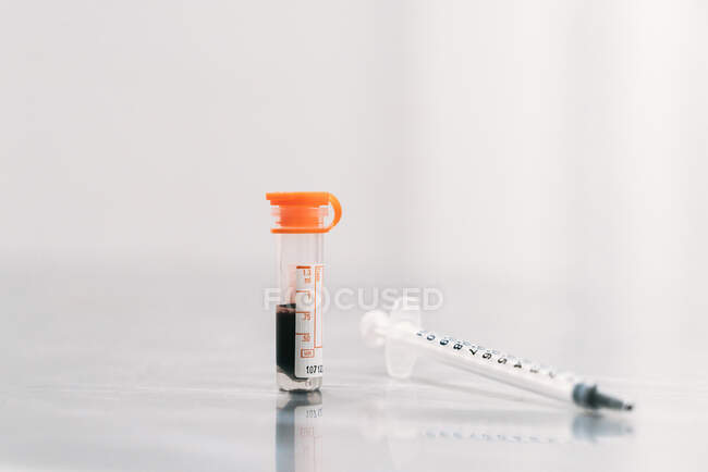 Стеклянная трубка с образцом крови пациента, лежащего возле шприца на столе в ветеринарной лаборатории — стоковое фото
