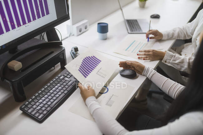 From above of crop unrecognizable female colleagues analyzing diagrams at table while working in modern workspace — Stock Photo