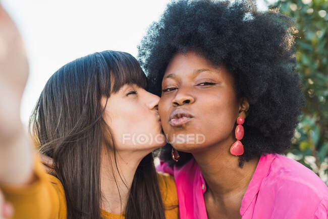 Amar a la mujer besar a la novia negra mientras toma uno mismo tiro en el parque de verano y disfrutar de fin de semana - foto de stock