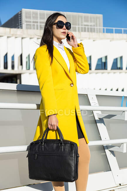 Asiatica donna d'affari con cappotto giallo che cammina sulla strada con edificio sullo sfondo — Foto stock