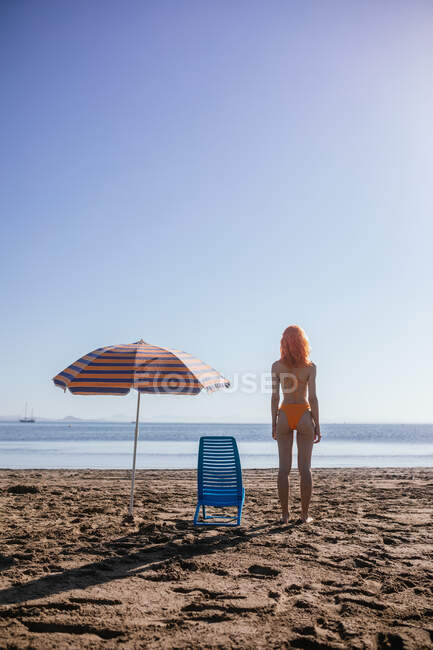 Visão traseira do anônimo jovem ruiva em pé na praia em um dia ensolarado no verão — Fotografia de Stock