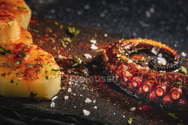 De cima de tentáculo de polvo frito e pedaços de batata servidos com especiarias em placa preta na mesa — Fotografia de Stock