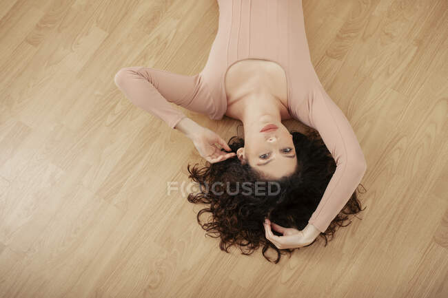 D'en haut de tendre femelle en body beige couché sur le sol en bois et regardant la caméra — Photo de stock