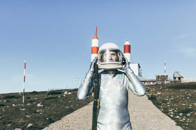 Старший чоловік у космосі знімає захисний шолом, стоячи на шляху біля космічного корабля з ракетними антенами у безхмарний день — стокове фото