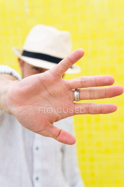 Unrecognizable guy in stylish summer outfit and hat doing no gesture and hiding face from camera against yellow wall — Stock Photo