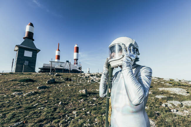 Side view man in spacesuit standing on rocky ground against metal fence and striped rocket shaped antennas on sunny day — Stock Photo