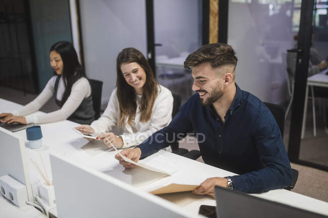 Gruppe fröhlicher multiethnischer Coworker sitzt am Tisch und liest Dokumente, während sie gemeinsam im Coworking Space arbeiten — Stockfoto