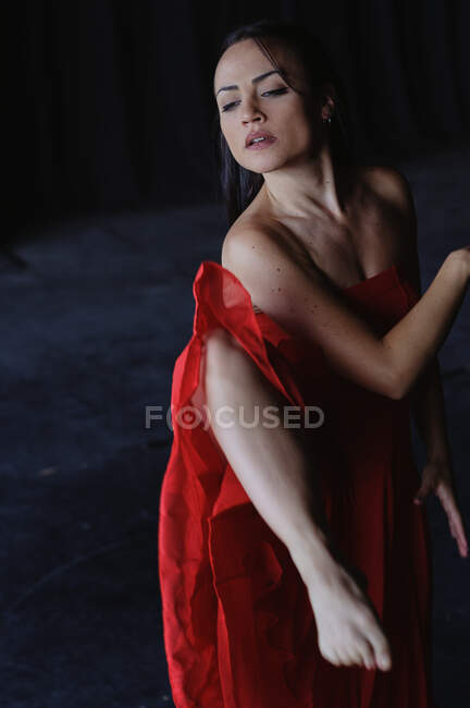 Young gentle woman in bright clothes dancing flamenco while looking down on dark background — Stock Photo