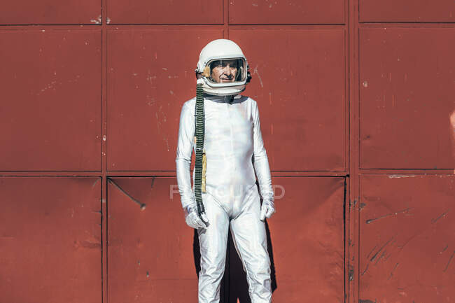 Человек в скафандре стоит возле красной стены промышленного объекта в солнечный день — стоковое фото